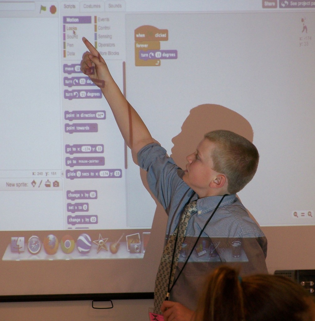 Photo of middle school student pointing to scratch computer program on a presentation screen